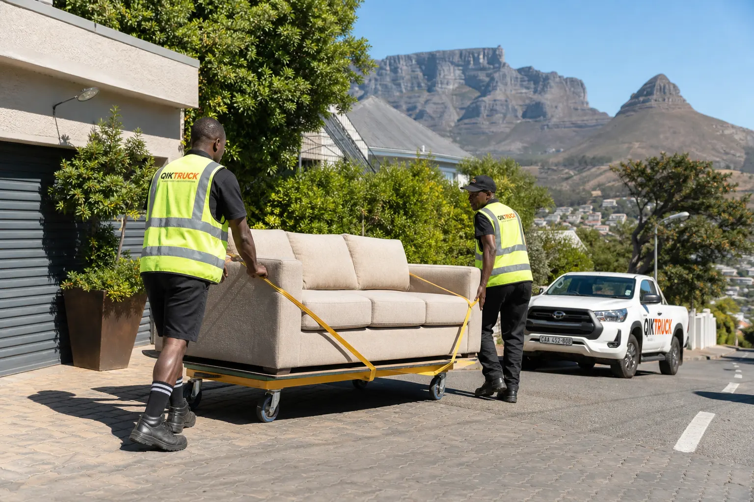 QikTruck crew rolling a sofa on a furniture trolley in Cape Town with Table Mountain behind