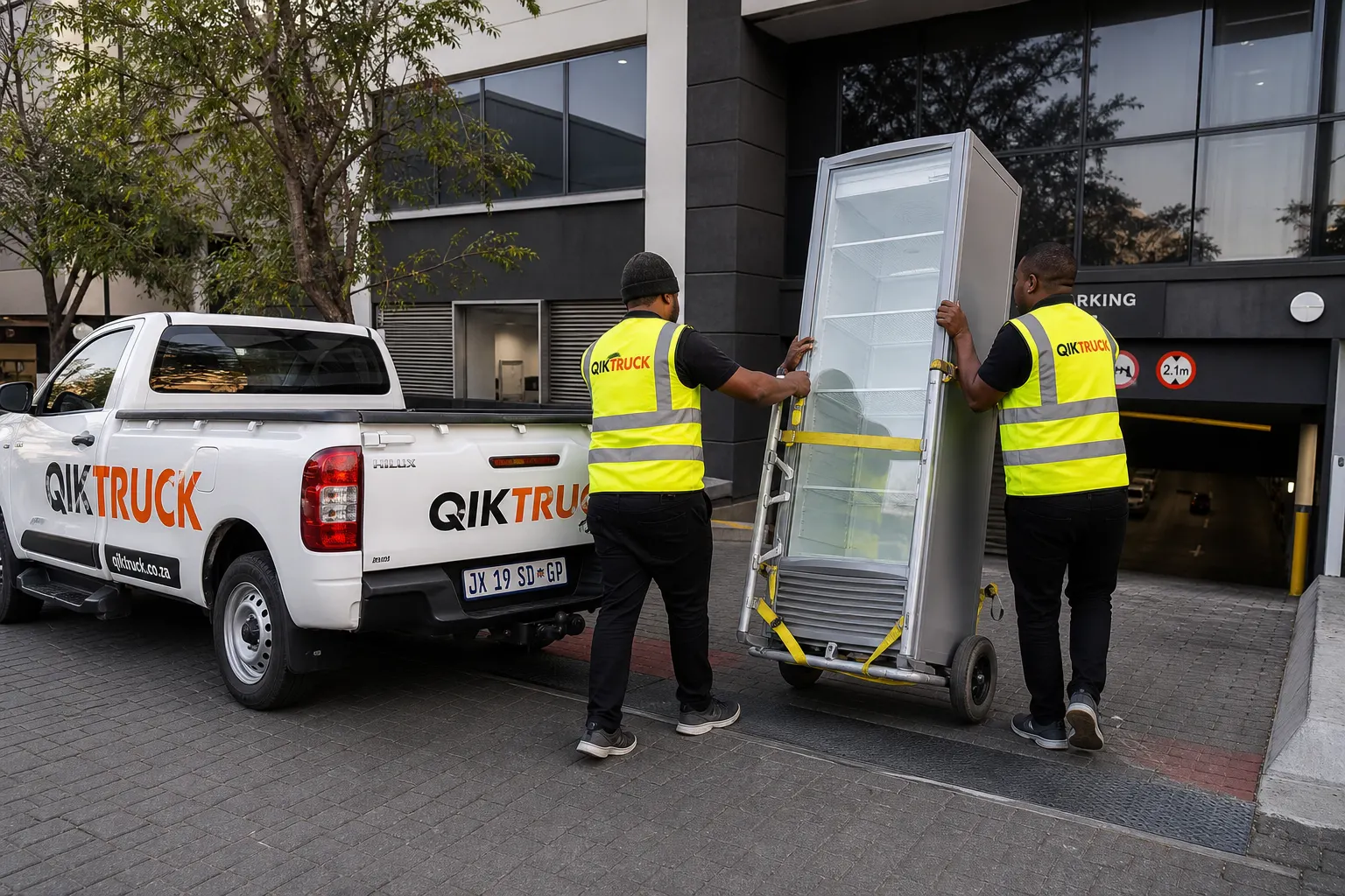 QikTruck crew rolling a fridge on an appliance trolley at a Sandton office park
